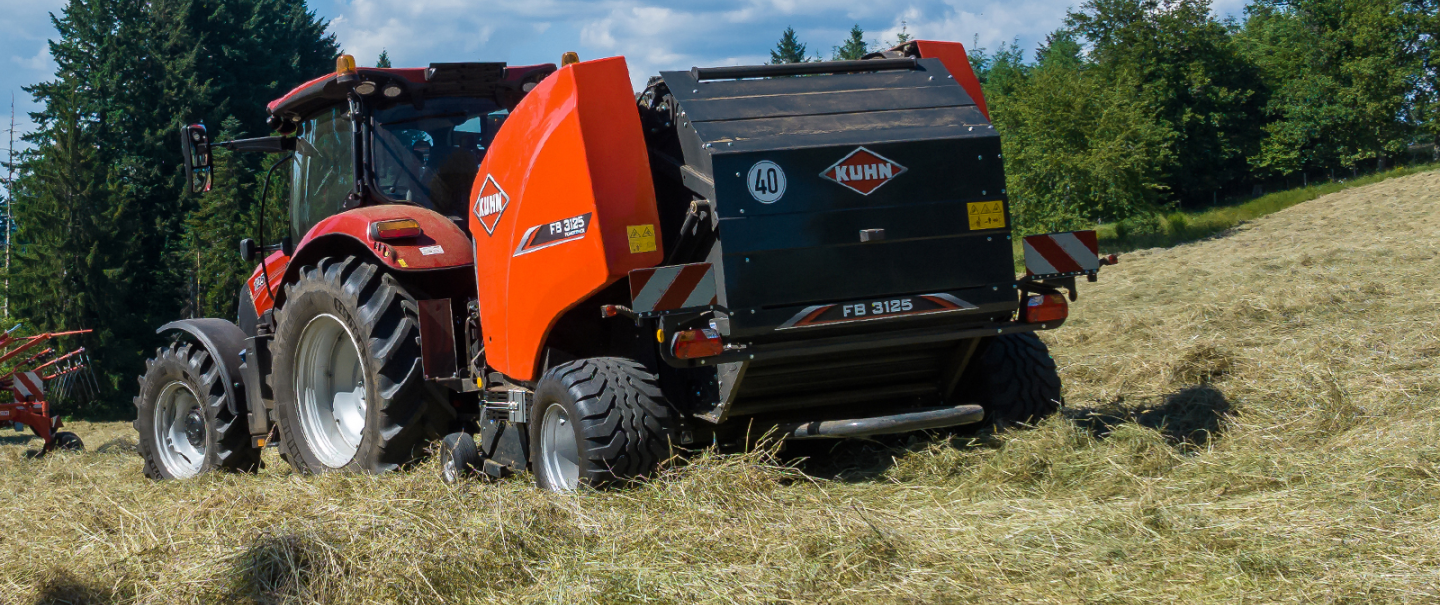 KUHN FB 3125 fixed round baler with the operator in the field in the background